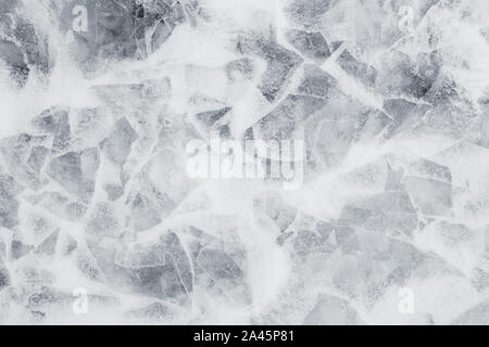 Close-up of snow on cracked and thin layers of ice in the winter. Simple and minimal full frame abstract background in black and white. Copy space. Stock Photo