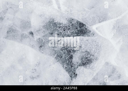 Close-up of snow on cracked and thin layers of ice in the winter. Simple and minimal full frame abstract background in black and white. Copy space. Stock Photo