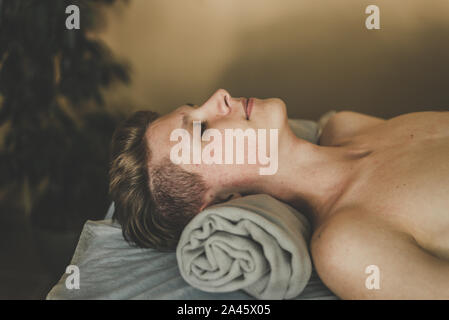 The man on the massage table is relaxing. The man before the massage feels calm and lies on a towel. Stock Photo