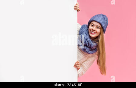 Blonde girl in winter hat staying next to blank board Stock Photo