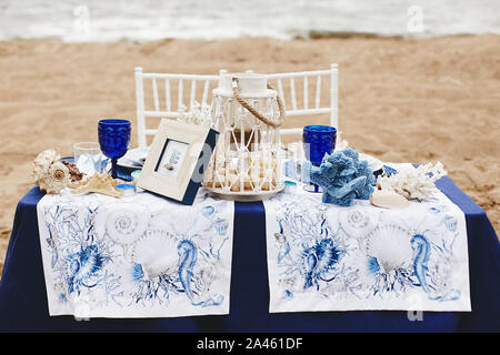 Wedding decoration in a marine style - table for the bride and groom on a sandy beach decorated with sea shells, corals, candlelight and wineglass Stock Photo