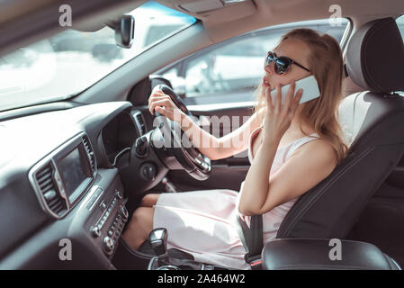 woman makes phone call, in summer city parking lot near shopping center, reversing in parking lot. Pink dress sunglasses listening to message on a Stock Photo