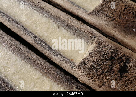 Process of production and crystallization of salt from sea water. Gutters hollowed into palm trunks. The sun evaporates sea water from wooden logs. Stock Photo