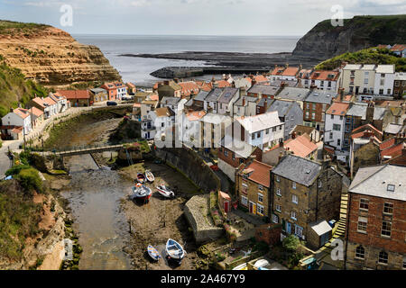 Overview of seaside village of Straithes houses and harbour with cliffs and boats at low tide on the North Sea North Yorkshire England Stock Photo