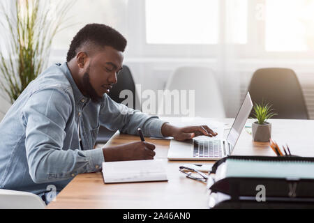 Employee using laptop and taking notes while working in office Stock Photo