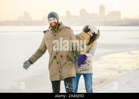 Young couple cheerfully flounders in snow. Between comic fight. Happy young couple hugs in winter snowy woods. Romantic lifestyle men and women in Stock Photo