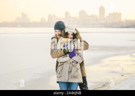 Young couple cheerfully flounders in snow. Between comic fight. Happy young couple hugs in winter snowy woods. Romantic lifestyle men and women in Stock Photo