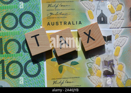 Tax in 3d wooden alphabet letters on a background of Australian one hundred dollar banknotes. Stock Photo