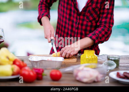 young man cutting vegetables for salad or barbecue grill during outdoor french dinner party near the river on beautiful summer evening in nature Stock Photo