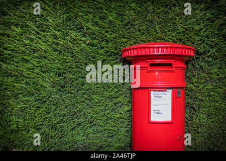 A Striking Red British Post Box Set Against A Neat Green hedgerow In England Stock Photo