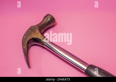 A worn, used metal hammer, placed diagonally across the frame with its handle extending outside, is against a pink background. Stock Photo