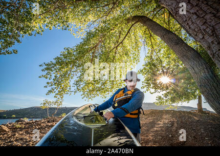 senior male is carrying a stand up paddleboard on a shore of mountain lake, action camera POV Stock Photo