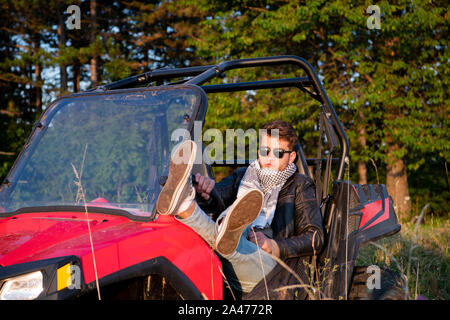 portrait of young happy excited man enjoying beautiful sunny day while driving a off road buggy car on mountain nature Stock Photo