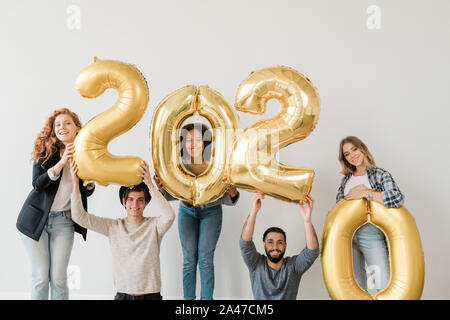 Happy teenagers standing along white wall while holding number of next year Stock Photo