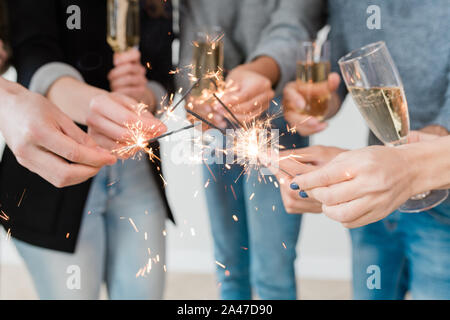 Hands of young friends holding burning bengal lights and flutes of champagne Stock Photo