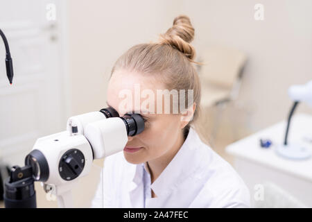 Young pretty eye doctor looking through optometric equipment Stock Photo