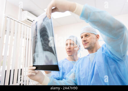 Young and mature doctors in uniform looking attentively at x-ray of lungs Stock Photo