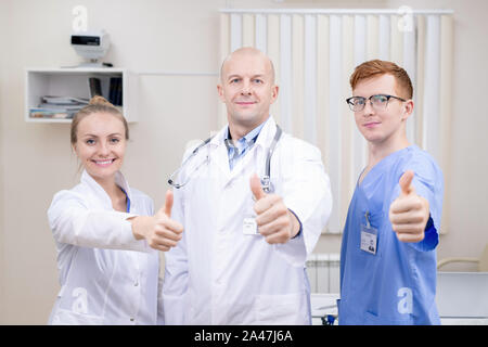 Three successful professionals in medical uniform showing thumbs up Stock Photo