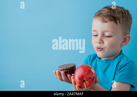 Portrait happy, smiling boy choosing junk food. Healthy versus unhealthy food. Healthy vs unhealthy eating, teenager choosing between cookie or an app Stock Photo