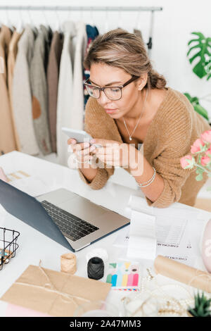 Pretty young casual shop assistant of modern boutique bending over workplace Stock Photo