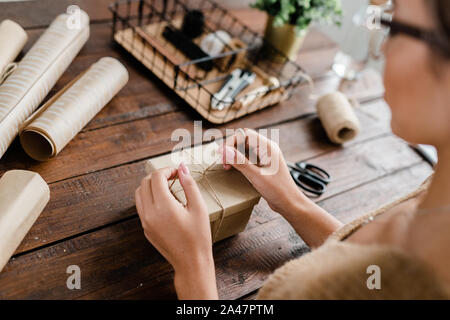 Hands of young female making knot on top of giftbox while packing gifts Stock Photo