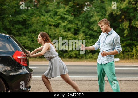 Young couple pushing broken car on road, breakdown Stock Photo