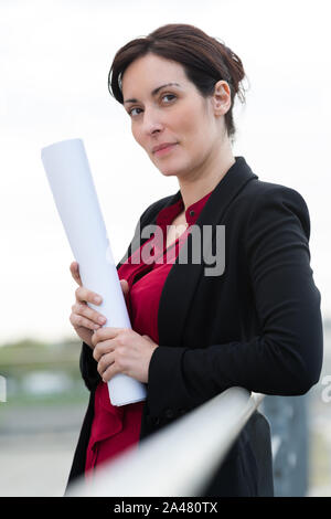 female architect studying drafts while visiting large construction site Stock Photo