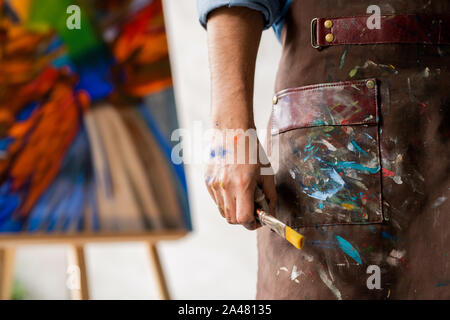 Part of professional painter in dirty apron holding paintbrush in hand Stock Photo