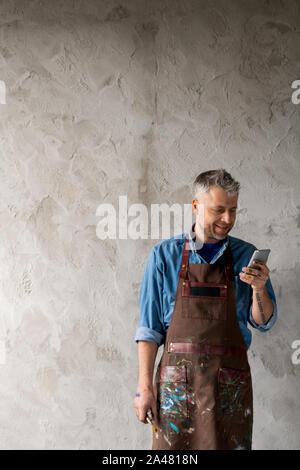 Happy middle aged professional painter in workwear scrolling in smartphone Stock Photo