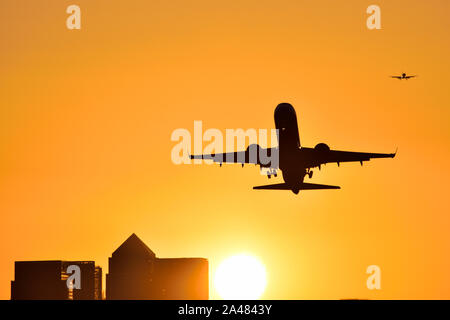 Plane taking off from London City airport with golden skies as the sun sets behind the Canary Wharf skyline Stock Photo