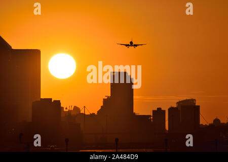 Plane landing at London City airport with golden skies as the sun sets behind the Canary Wharf skyline Stock Photo