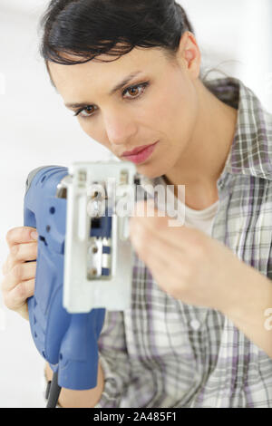serious middle-aged professional female carpentry fixing an electric drill Stock Photo