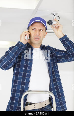 man installing cctv camera taking call on his smartphone Stock Photo