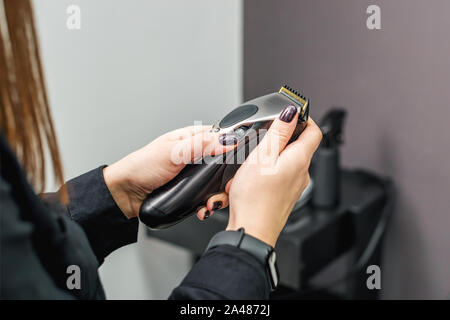 Hair trimmer machine for hairstyles in the hands of hairdresser. Woman's hands holds a hair clipper machine on the background of a hairdresser salon. Stock Photo