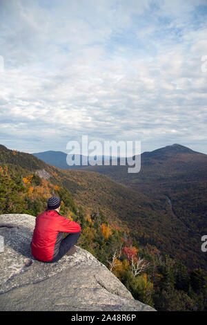 Hiker on Table Rock trail summit, looking down over cliff edge, Grafton Notch State Park, Maine, October Stock Photo