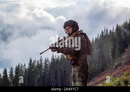 Chilliwack, British Columbia, Canada - October 5, 2019: Army Man wearing Tactical Uniform and holding Machine gun in the Outdoor Mountains during fall Stock Photo