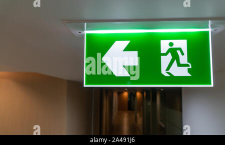 Green fire escape sign hang on the ceiling in the office. Stock Photo