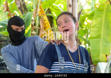 Man with masked robber and threatening with gun to scared woman in car parking. The victim of the crime was terrified and have anxiety symptoms. Stock Photo