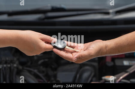 Close up of customer hand giving car key to car engine repairman on car engine background to repair it . Concept of maintenance vehicle mechanic and a Stock Photo