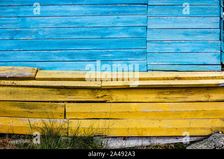 multi-colored blue and yellow boards like Ukraine flag make up the wall of an old house on a rocky ground with grass Stock Photo