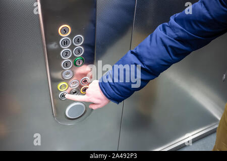 man in a blue jacket in the elevator presses his finger on the button to close the door Stock Photo