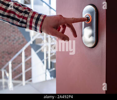 finger presses the elevator button down on the background of the stairs in a plaid shirt Stock Photo