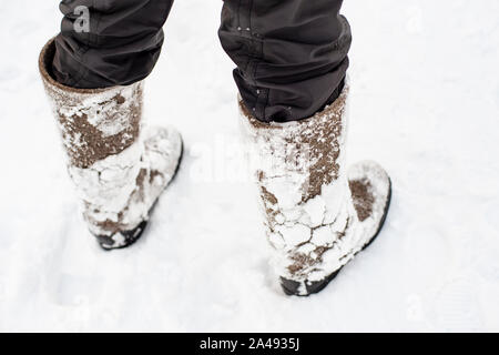 Feet in warm, comfortable felt shoes with snow stuck to them after a walk through the snowdrifts in the forest are on the cleared road. The traditiona Stock Photo