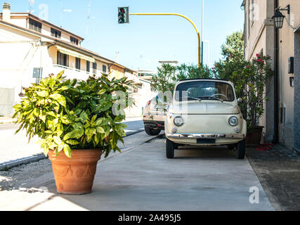 Small vintage italian car. Beige color old car in front of old house facade and flowers.. Stock Photo