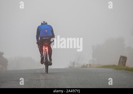 Flintshire, North Wales, UK 13th October 2019. UK Weather:  A deluge of torrential rain will full over the UK with many parts under heavy rain showers and in some places fog.  A cyclist heading into the fog near the village of Moel-y-Crio with bike lights iluminated for safety © DGDImages/AlamyLiveNews Stock Photo