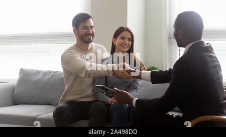 Smiling young married couple shaking hands with african american realtor. Stock Photo