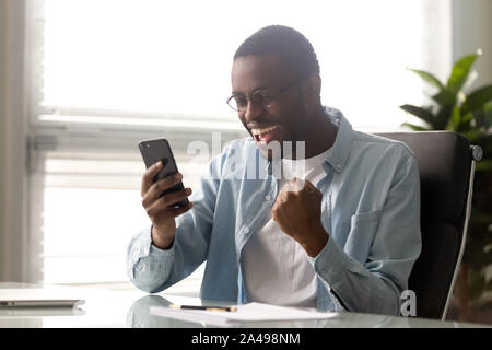 Euphoric millennial african american businessman looking at mobile phone screen. Stock Photo