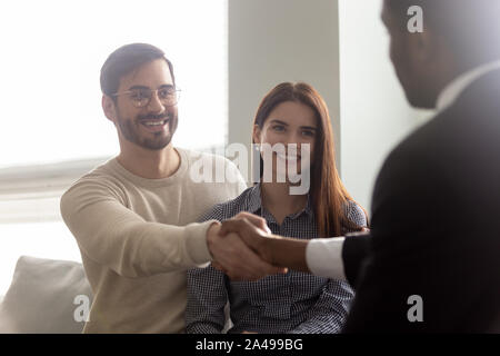 Excited millennial husband shaking hands with african american male broker. Stock Photo
