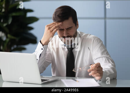 Frustrated young manager suffering from strong head ache. Stock Photo