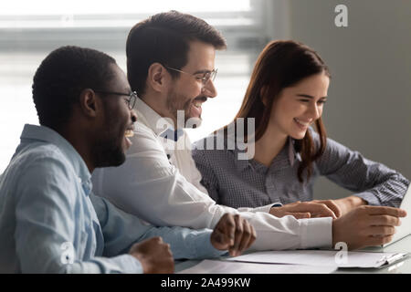Overjoyed multiracial teammates watching funny video together. Stock Photo